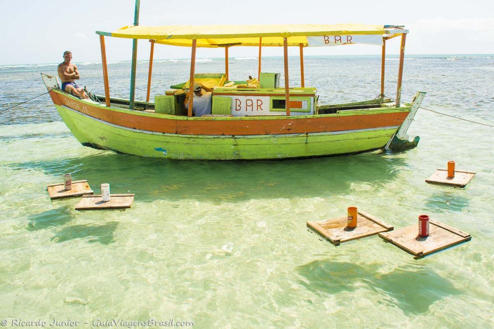 Imagem  de um barco de pescador que é um bar nas águas da piscina natural de Moreré.